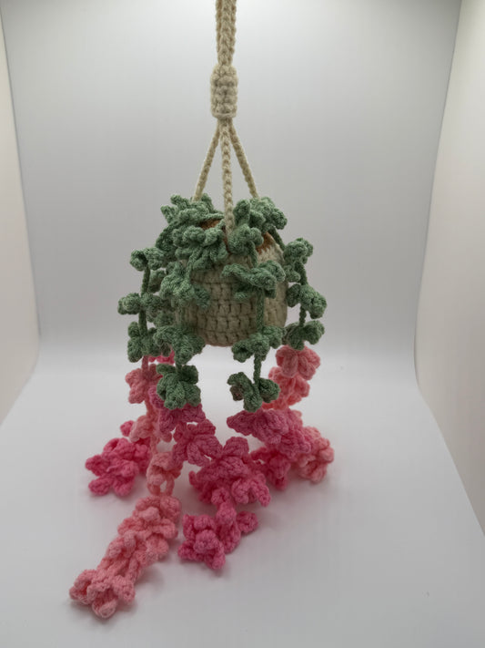 Crocheted plant holder with pink and green elements on a white background